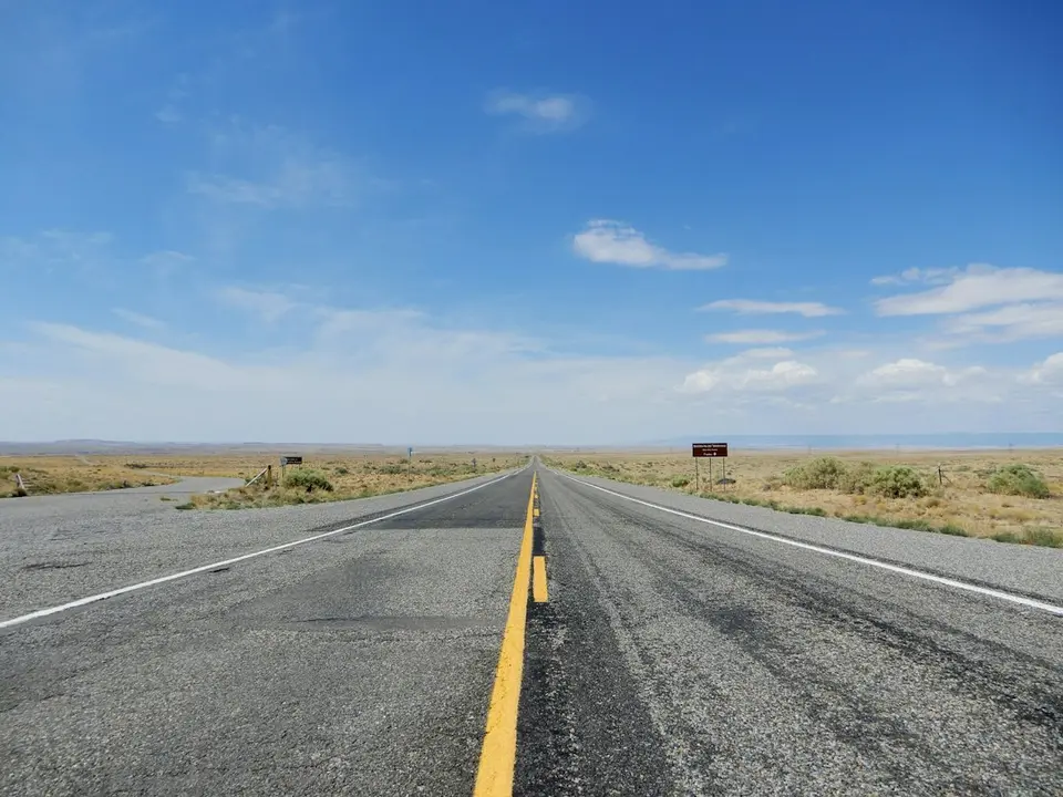 Rechte Mexicaanse weg met gele middenlijn die door een droog landschap loopt onder een heldere hemel.