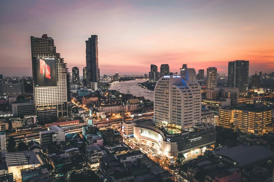 Skyline de Bangkok au crépuscule avec immeubles illuminés, fleuve et ciel coucher de soleil vue depuis un balcon en hauteur.