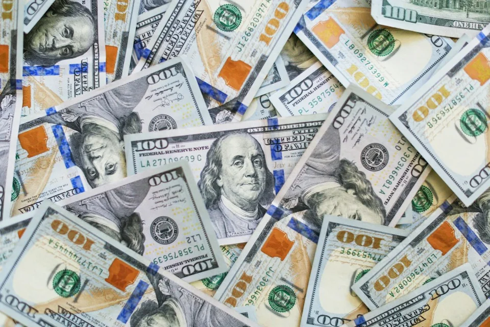 Billets de dollars américains de différentes coupures éparpillés sur une surface blanche.