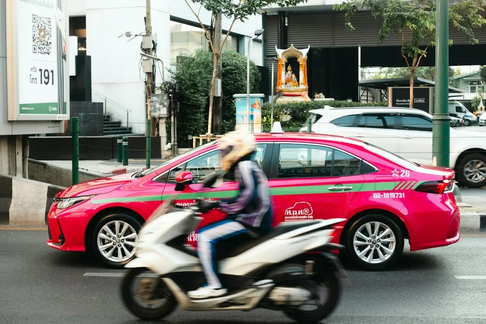 Livreur à moto transportant des colis dans une rue de Bangkok avec arrière-plan urbain.