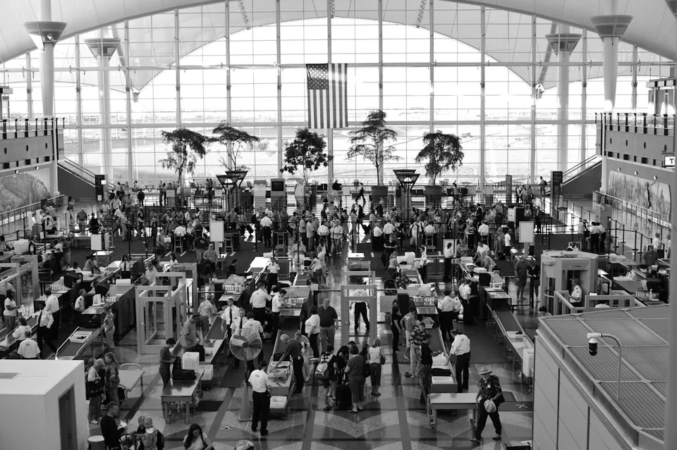 Überfüllte Flughafenhalle mit Reisenden und Gepäck in einem modernen Terminal mit großen Fenstern.