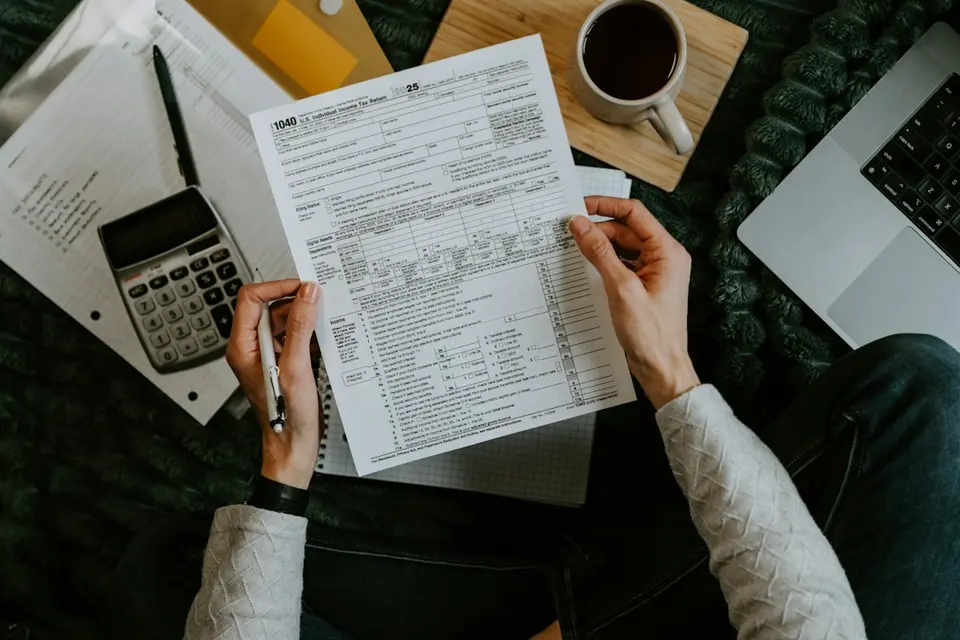 Mains tenant un formulaire fiscal IRS 1040 avec calculatrice et café sur un bureau