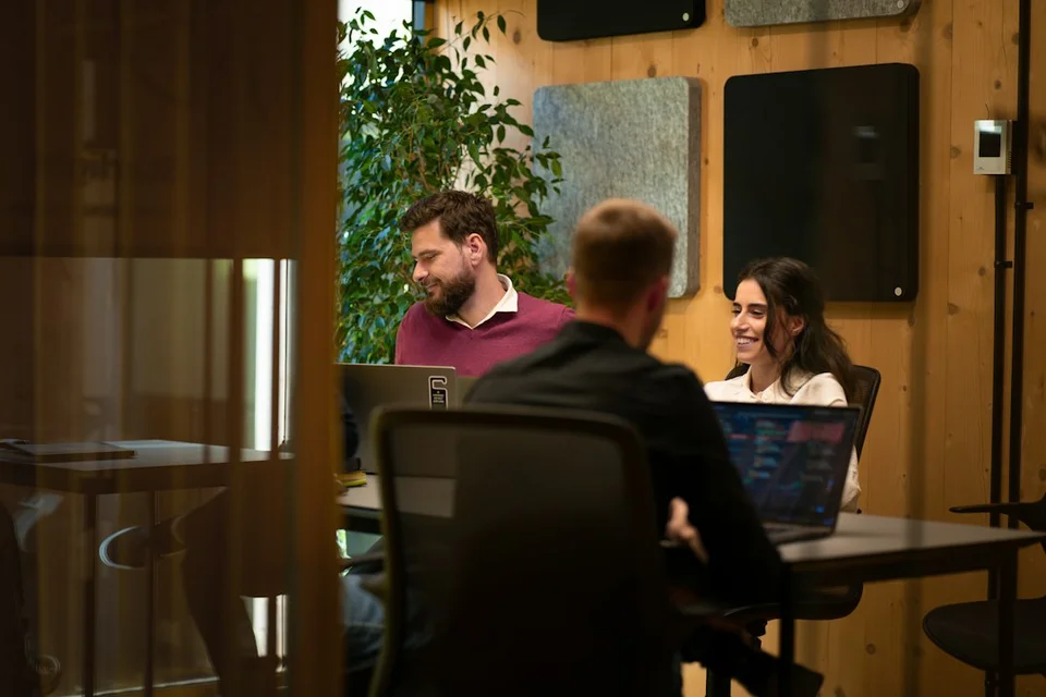Digital nomads working on laptops in a bright, modern coworking space with wooden walls and plants.