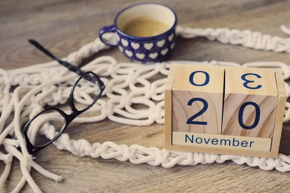 Wooden calendar showing November 20 on a desk with a coffee cup and glasses.