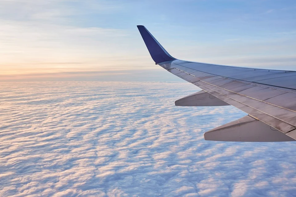 Airplane wing above the clouds at sunset, seen from the window.