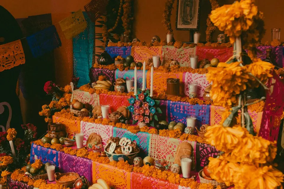 Altar tradicional do Dia de Muertos com flores de cempasúchil, velas, tecidos coloridos e decorações religiosas.