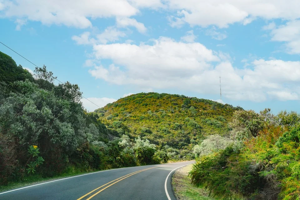Kronkelige bergweg met tropische begroeiing in Costa Rica onder een blauwe lucht met witte wolken.