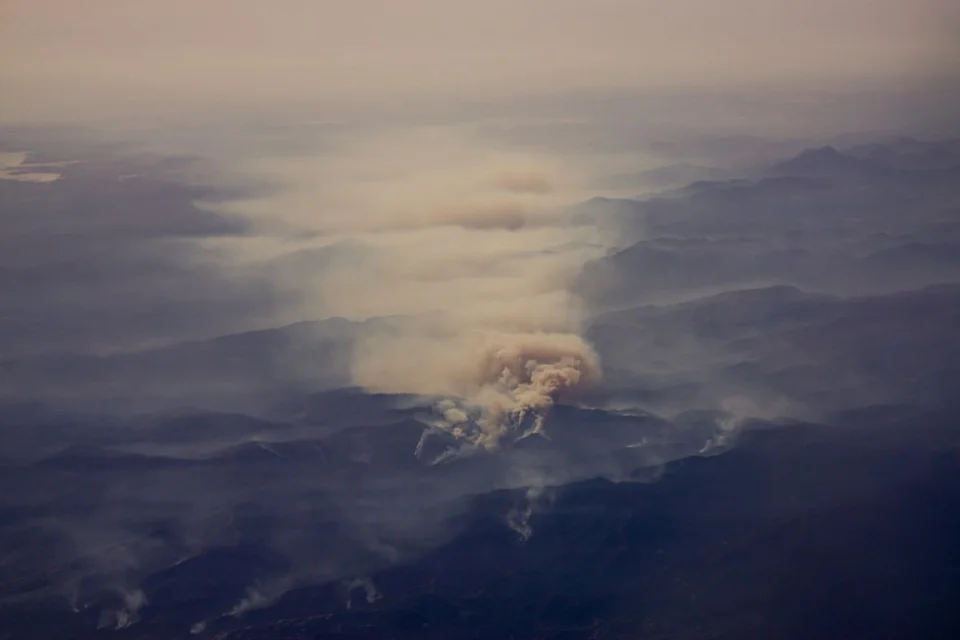 Aerial view of smoke plumes rising from a forest fire above dry, wooded hills in Spain.
