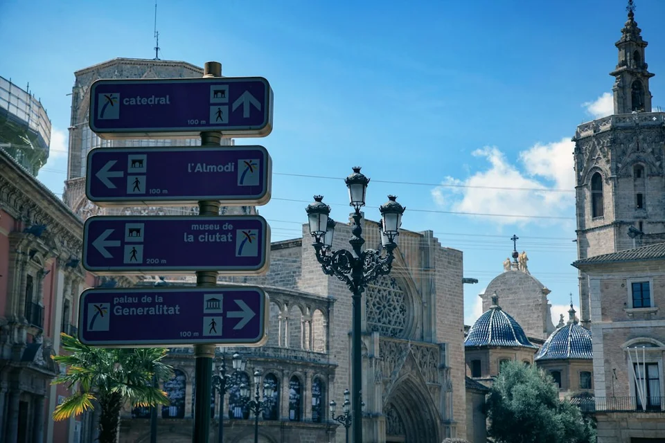 Sunny historic center of Valencia with pale facades, directional signs and a visible cathedral tower.