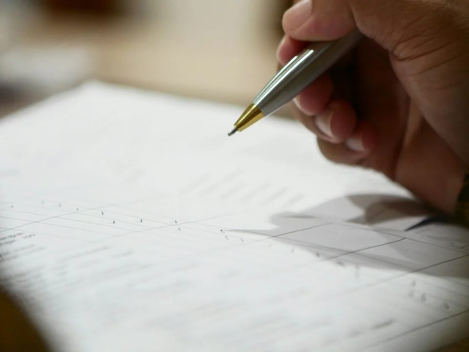 Hand holding a pen about to sign a document on lined paper.