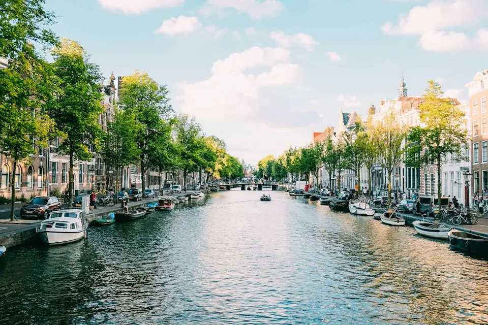 Traditionele trapgeveltjes langs een Amsterdamse gracht, met aangemeerde boten en straten met bomen.
