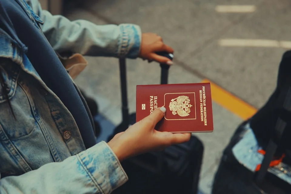 Person holding a red passport with a suitcase, getting ready to travel abroad.
