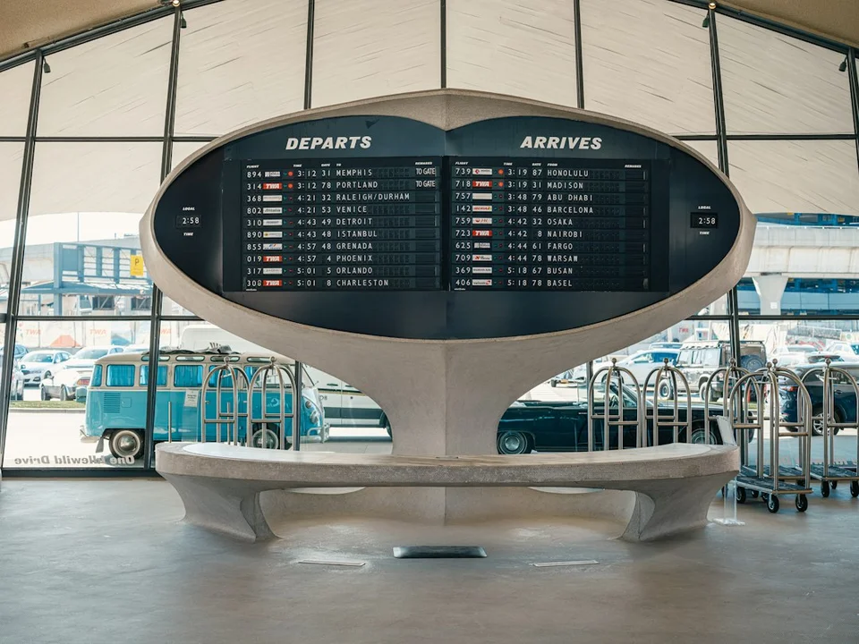 Airport departures and arrivals display board with luggage trolleys below.