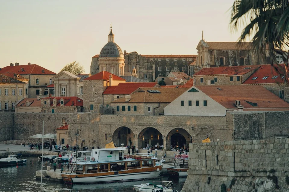 Croatian coastal old town with red roofs, stone walls, a church dome and boats in the harbor.