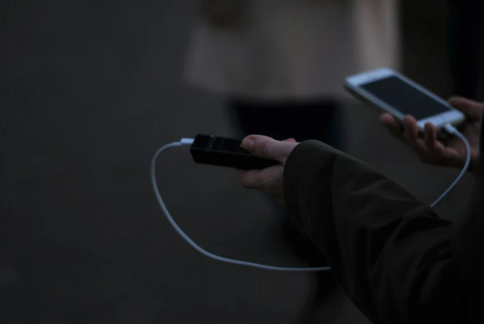 Personne tenant une batterie externe connectée à un smartphone via câble USB pour la recharge.