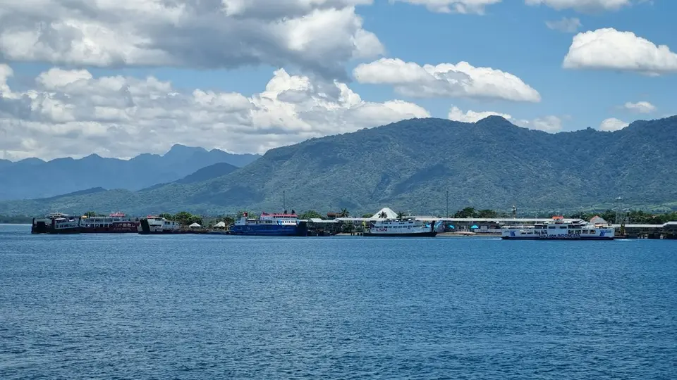 Indonesische haven met aangemeerde veerboten en bergachtige kust onder een blauwe lucht