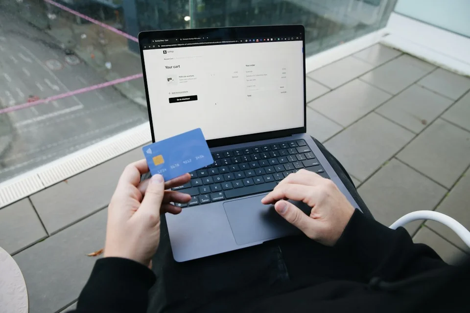 Person holding a blue bank card while entering payment details on a laptop for an online booking.