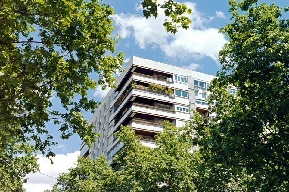 Modern residential building with balconies surrounded by greenery and blue sky.