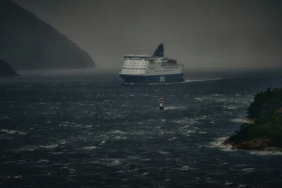 Een ferry die door ruwe zee vaart tijdens onweer langs een rotsachtige kust.