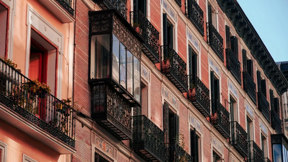 Pink residential building with ornate balconies and windows on a street in a Spanish city.