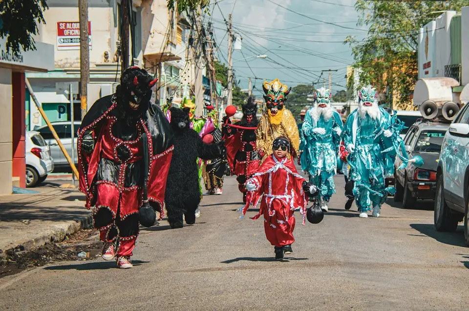 Défilé d'Halloween avec des participants en costumes élaborés rouge, noir et turquoise marchant dans une rue.