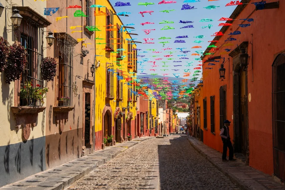 Colorful colonial street in Mexico with painted facades, cobblestones, and decorative banners strung overhead.