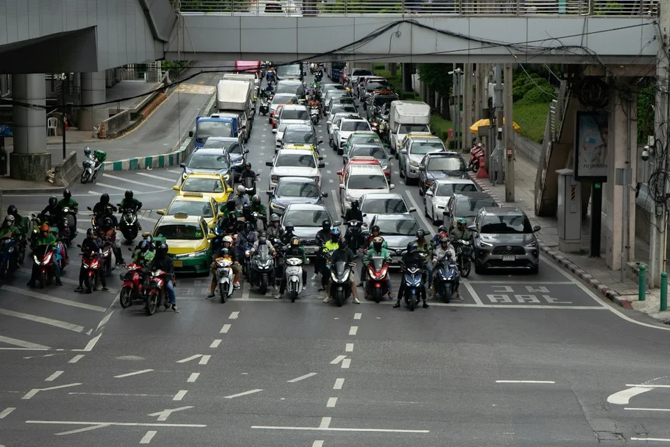 Thai motorcycles and scooters waiting at a red light on a crowded city street.