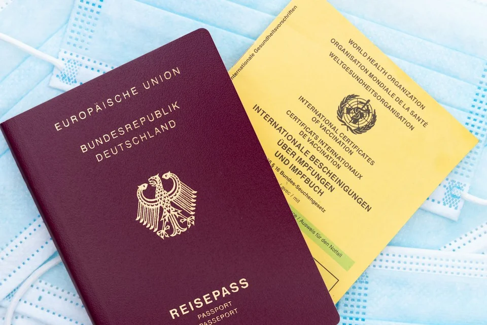 Passeport allemand et carnet de vaccination jaune sur surface bleue, illustrant les documents de voyage.