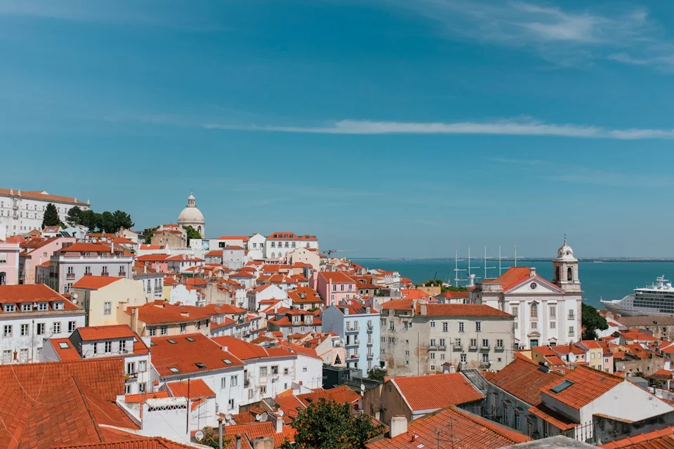 Lisbon cityscape with terracotta rooftops, white buildings and a view of the waterfront.