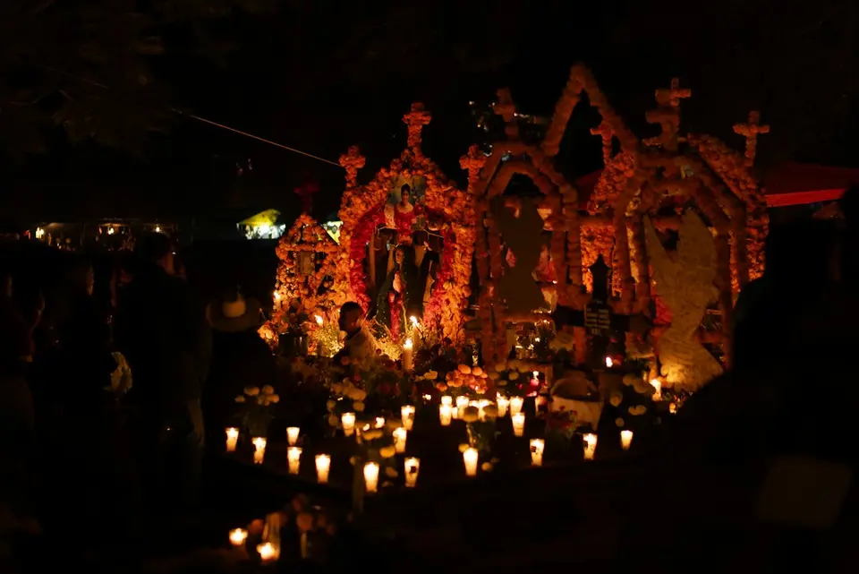 Altar for the dead decorated with marigolds and candles lit at night, visitors gathered around it.