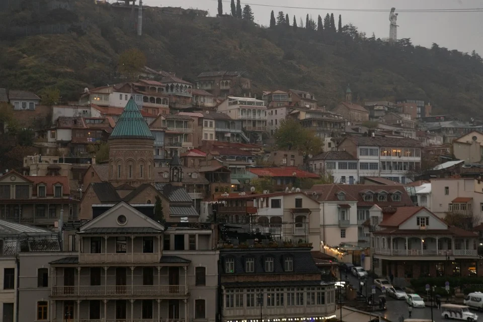 Rooftops and balconies of Old Tbilisi with a church dome on the hill, under cloudy light.